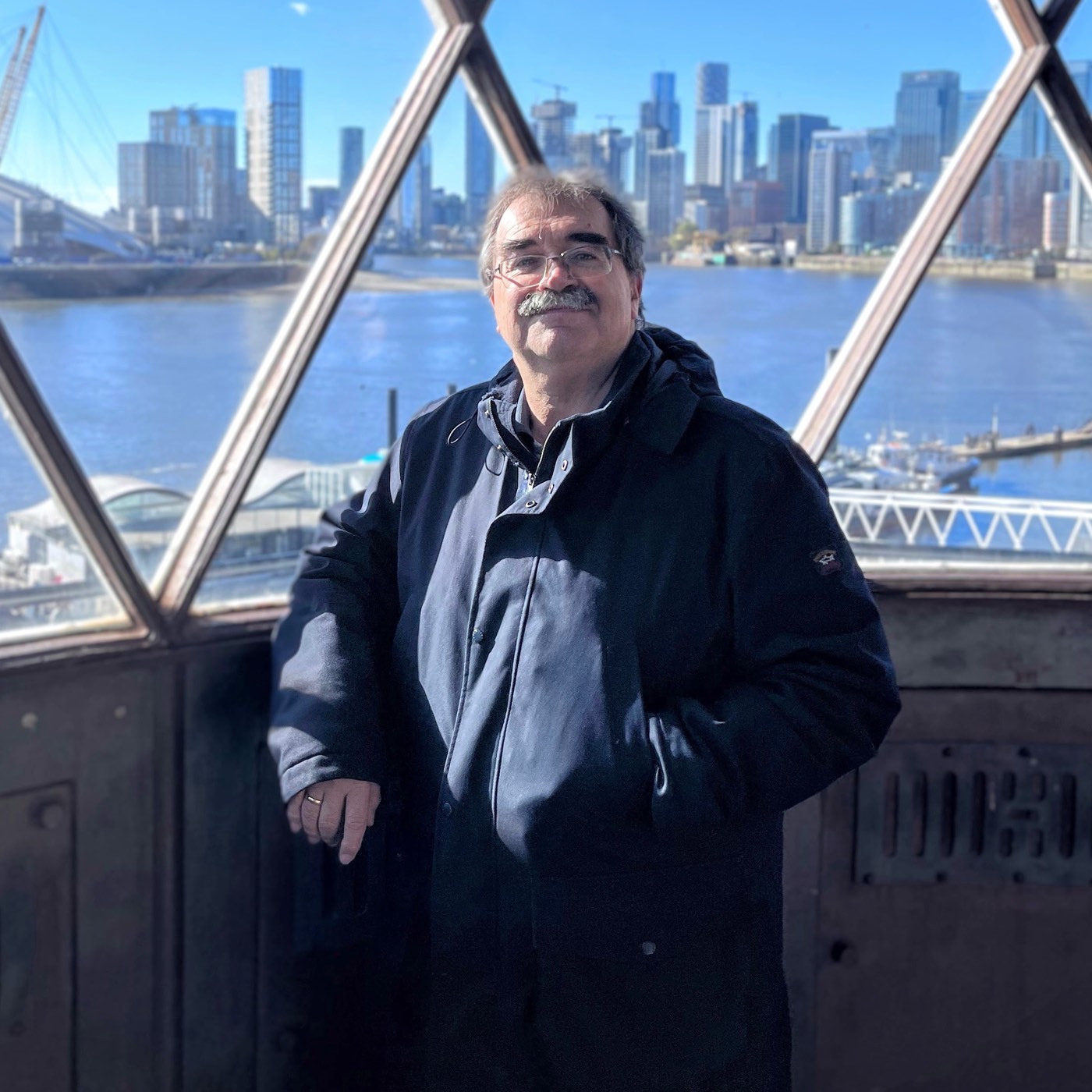 Titus Bihl vor einer Fensterfront mit Blick über die Themse auf die Hochhäuser von Canary Wharf.
